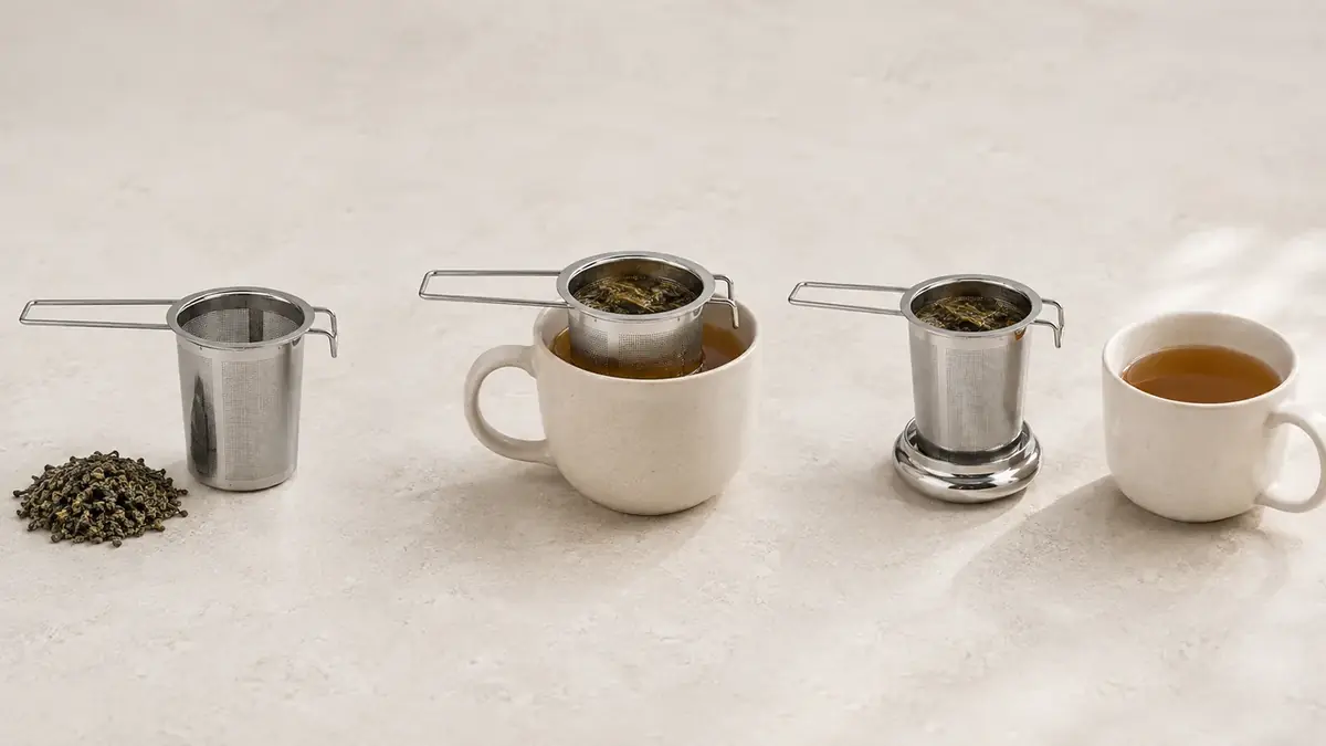 Three stages of brewing side by side: an empty basket with dry leaves, the basket steeping on a mug, and the basket resting on its upturned lid beside a finished cup