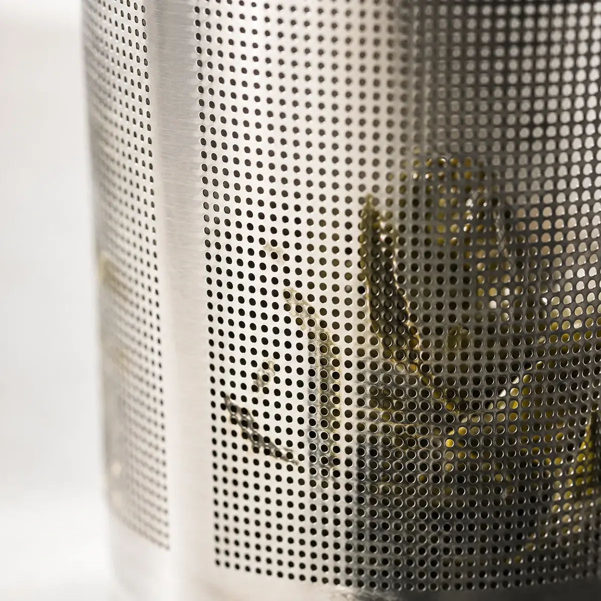 Extreme close-up of the fine perforated mesh of the steel basket with green leaves behind it
