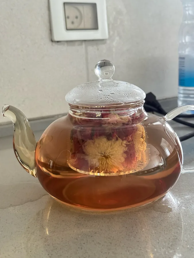 A blooming tea flower fully open inside the glass teapot, amber tea around it. Photographed by M***a, a verified buyer